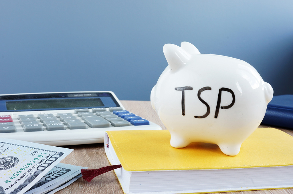 A desk with money, a calculator, a book, and a piggy bank with “TSP” written on it to represent TSP investment options