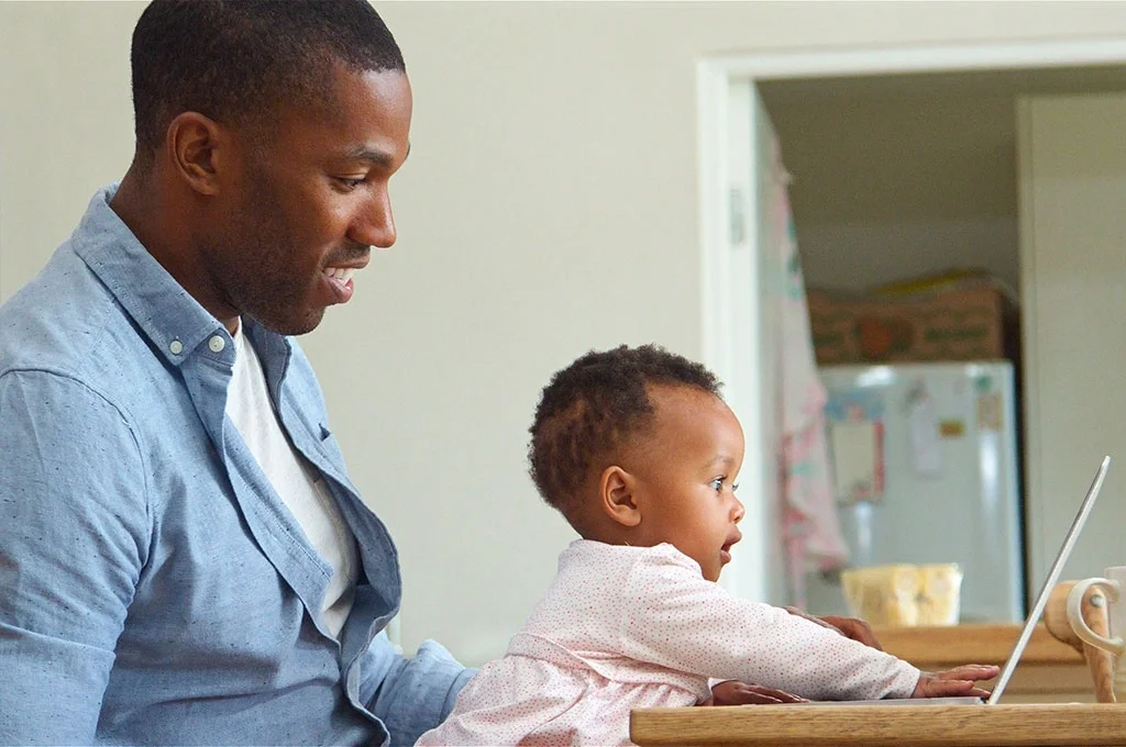 A father and his daughter sit at a table using a laptop