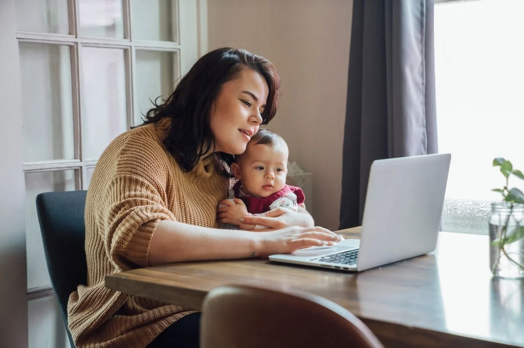A retired Army veteran searches at home for the best banks for veterans with her baby in her lap