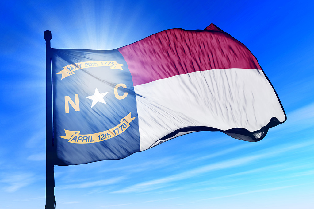 The North Carolina state flag waving with a blue sky and sun in the background