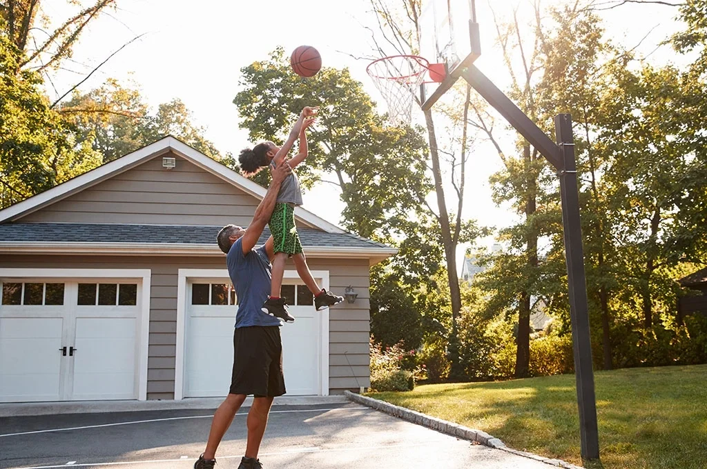 A veteran father lifting his child towards a basketball goal