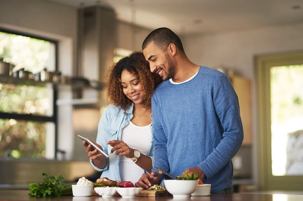 A veteran and his wife examine their finances while he prepares food in their kitchen