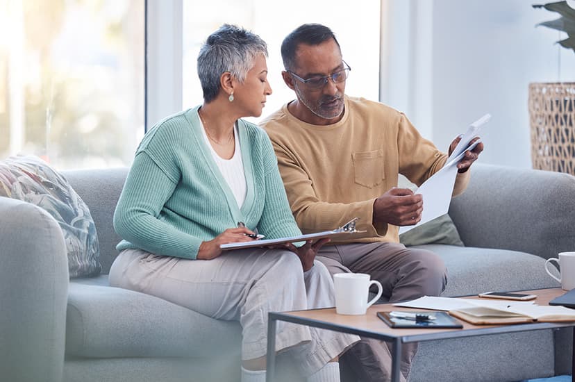A couple on the sofa going over financial documents to represent life insurance for veterans.