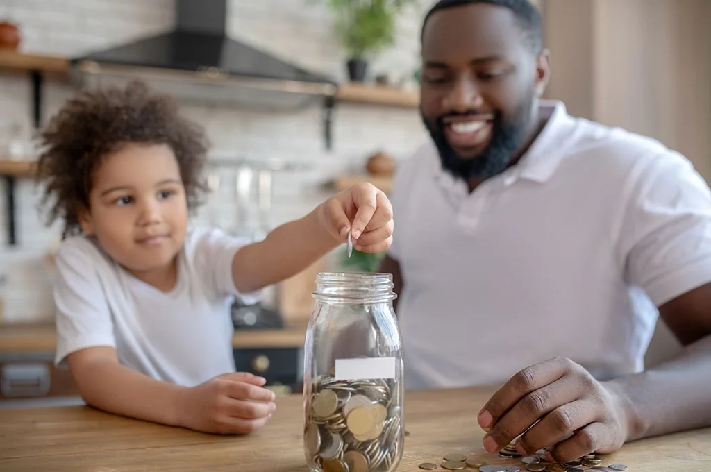 Veteran father putting coins in a jar wtih his child
