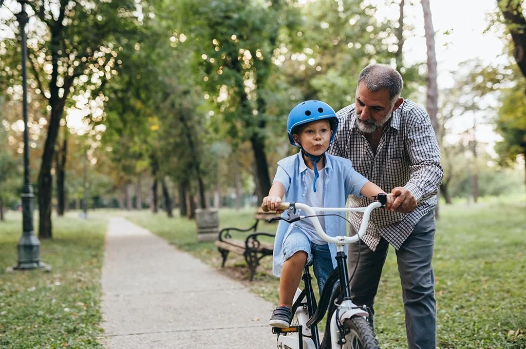 A grandfather teaching his grandson to ride a bike at the park