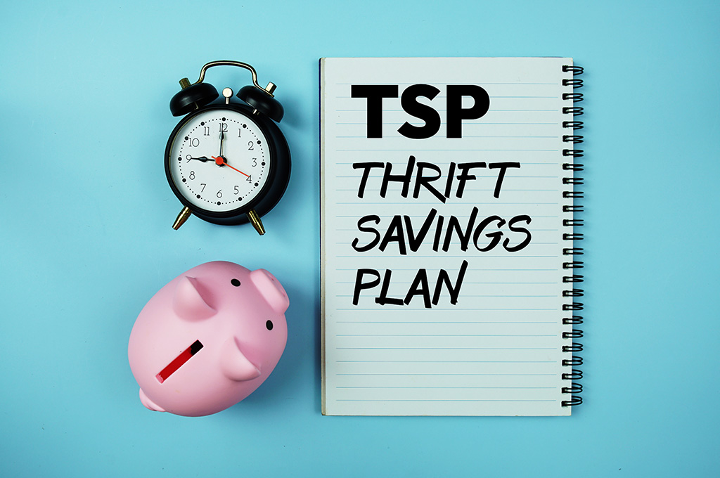 “Thrift Savings Plan” written on a notebook next to a piggy bank and an alarm clock